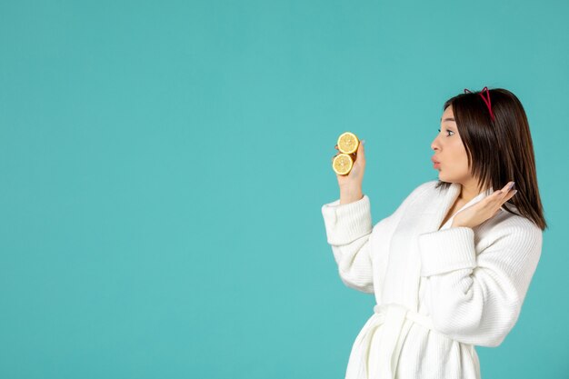 vista frontale giovane donna in accappatoio con limoni a fette su sfondo blu