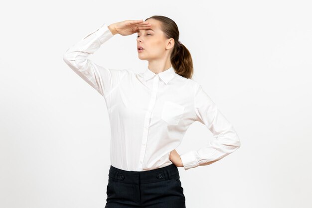 Vista frontale giovane donna in camicetta bianca guardando a distanza su sfondo bianco lavoro d'ufficio emozione femminile modello di sentimento feeling