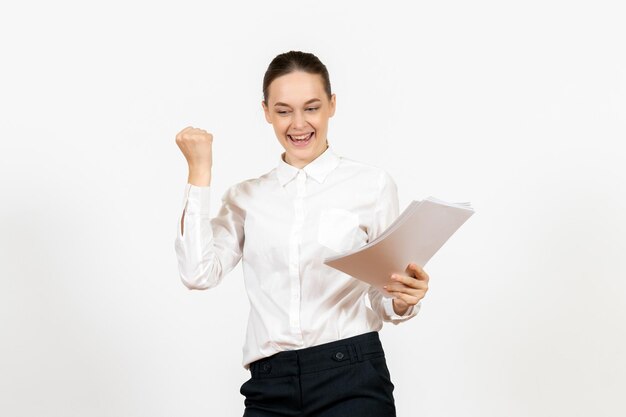 Vista frontale giovane donna in camicetta bianca in possesso di documenti e sorridente su sfondo bianco lavoro femminile emozioni sensazione ufficio