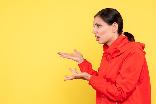 Vista frontale giovane donna in cappotto rosso su sfondo giallo