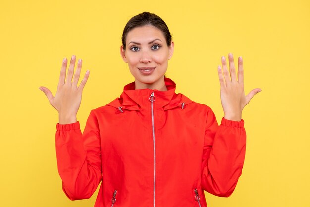 Vista frontale giovane donna in cappotto rosso su sfondo giallo