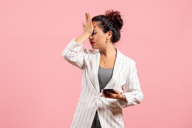 Vista frontale giovane donna in giacca bianca che tiene il telefono su sfondo rosa moda donna emozione sensazione signora colore