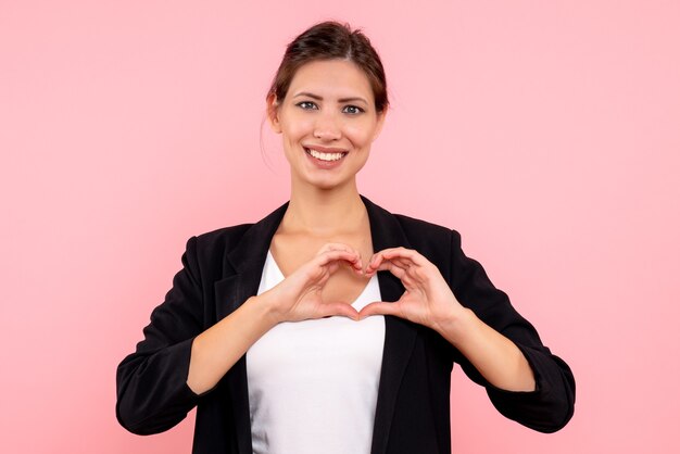 Vista frontale giovane donna in giacca scura sorridente e invio di amore su sfondo rosa