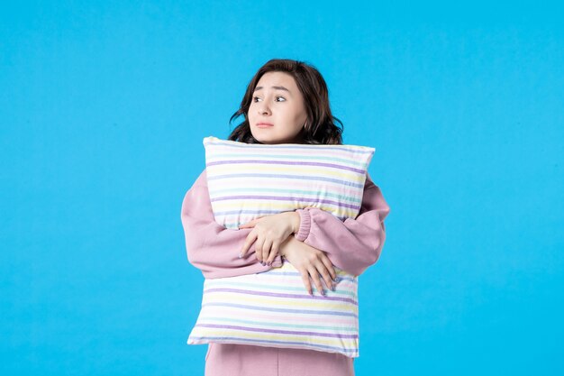 Vista frontale giovane donna in pigiama rosa che tiene cuscino sulla parete blu notte colore riposo a letto sonno emozione modello donna