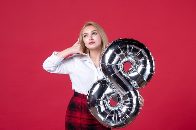 Vista frontale giovane donna in posa con palloncino d'argento come simbolo di marzo su sfondo rosso uguaglianza sensuale femminilità femminile affettuoso colore del giorno delle donne