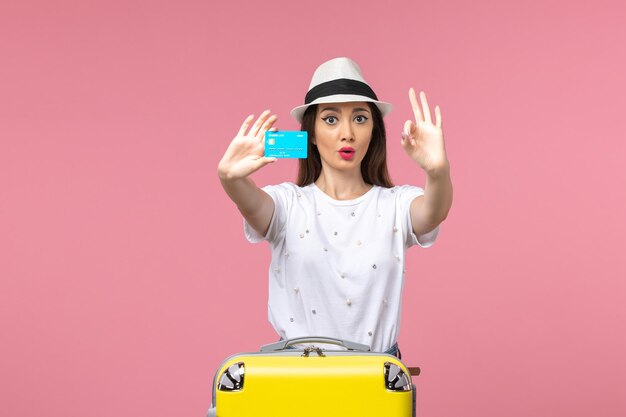 Vista frontale giovane donna in possesso di carta di credito blu sul viaggio di viaggio a parete rosa chiaro summer