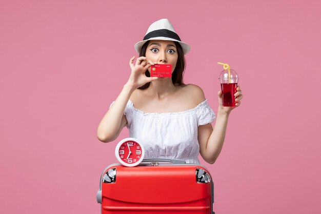 Vista frontale giovane donna in possesso di carta di credito e succo di frutta in vacanza sul pavimento rosa viaggio viaggio vacanze estive woman