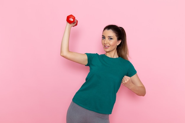 Vista frontale giovane donna in possesso di manubri e sorridente sul muro rosa atleta sport esercizio fisico allenamenti