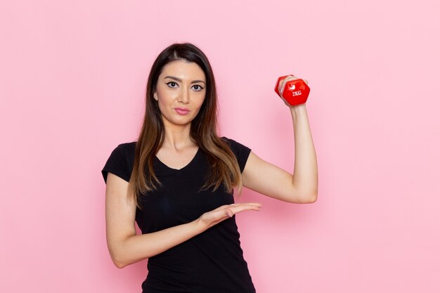 Vista frontale giovane donna in possesso di manubri sul muro rosa chiaro atleta sport esercizio salute allenamento