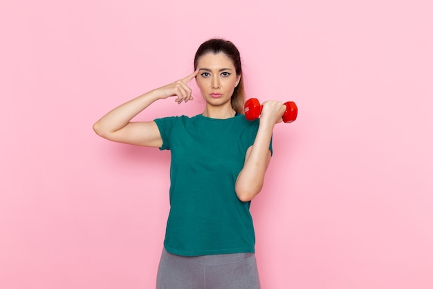 Vista frontale giovane donna in possesso di manubri sulla parete rosa chiaro atleta sport esercizio fisico allenamenti