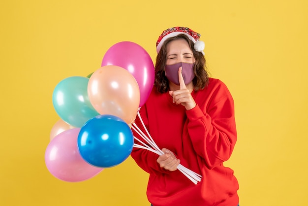 Vista frontale giovane donna in possesso di palloncini in maschera su giallo