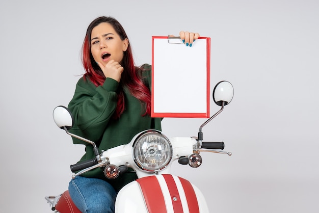 Vista frontale giovane donna sulla moto che tiene nota per la firma sul muro bianco