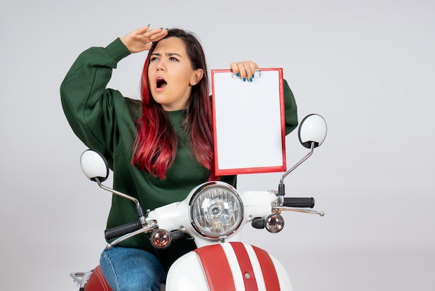 Vista frontale giovane donna sulla moto che tiene nota per la firma sul muro bianco