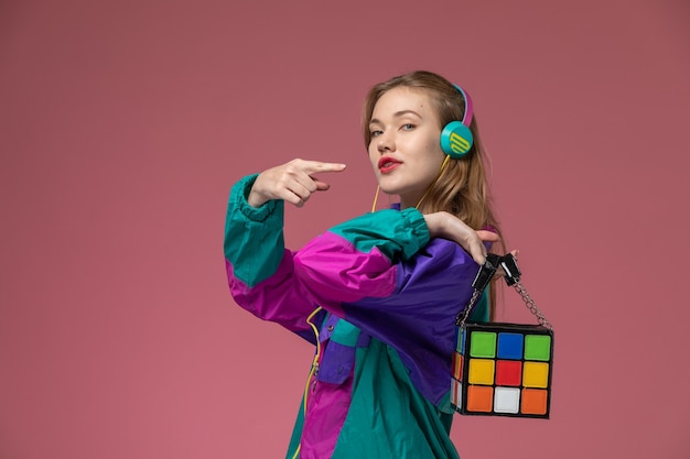 Vista frontale giovane femmina attraente che indossa cappotto colorato ascoltando musica sulla parete rosa scuro modello colore femmina giovane ragazza