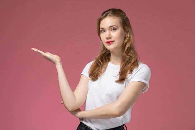 Vista frontale giovane femmina attraente in maglietta bianca in posa con gesti delle mani sulla parete rosa modello femmina posa foto a colori