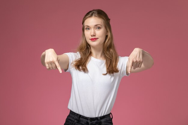 Vista frontale giovane femmina attraente in maglietta bianca in posa e sottolineando sul muro rosa modello femmina posa foto a colori femmina giovane