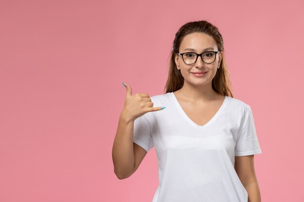 Vista frontale giovane femmina attraente in maglietta bianca smi e alzando una mano sullo sfondo rosa