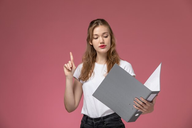 Vista frontale giovane femmina attraente in posa e lettura di file grigio sul muro rosa modello colore femmina giovane