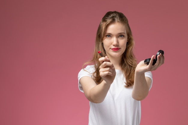 Vista frontale giovane femmina attraente in t-shirt bianca che tiene rossetto con il sorriso sul muro rosa modello colore femmina giovane