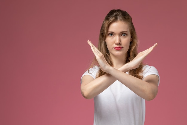 Vista frontale giovane femmina attraente in t-shirt bianca in posa mostrando segno di divieto sulla parete rosa modello femmina posa foto a colori