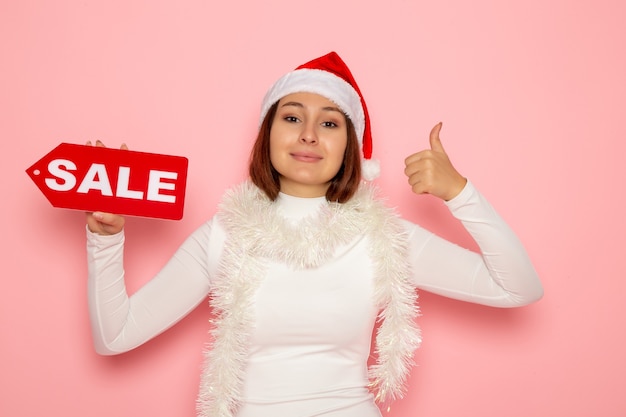 Vista frontale giovane femmina azienda vendita figura scritta sulla parete rosa colori vacanza capodanno moda neve natale