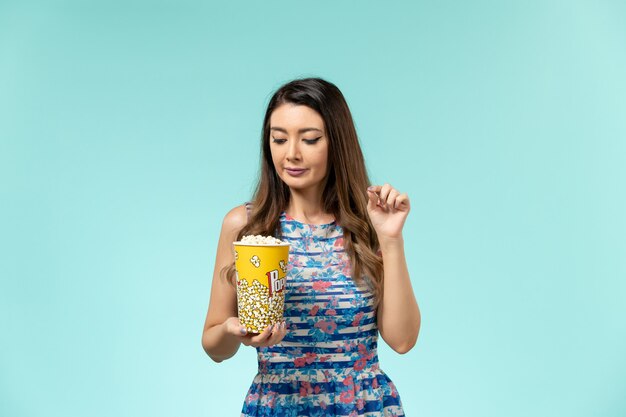 Vista frontale giovane femmina che tiene pacchetto di popcorn sulla superficie azzurra