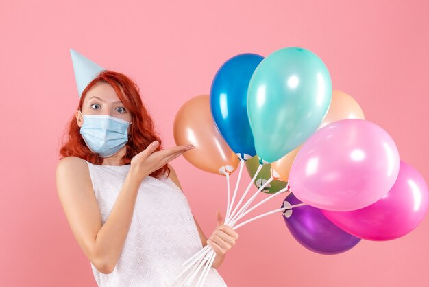 Vista frontale giovane femmina che tiene palloncini colorati in maschera sul rosa