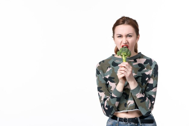 Vista frontale giovane femmina che tiene piccoli broccoli verdi e li morde su sfondo bianco piatto pranzo corpo salute cibo insalata orizzontale pasto dieta