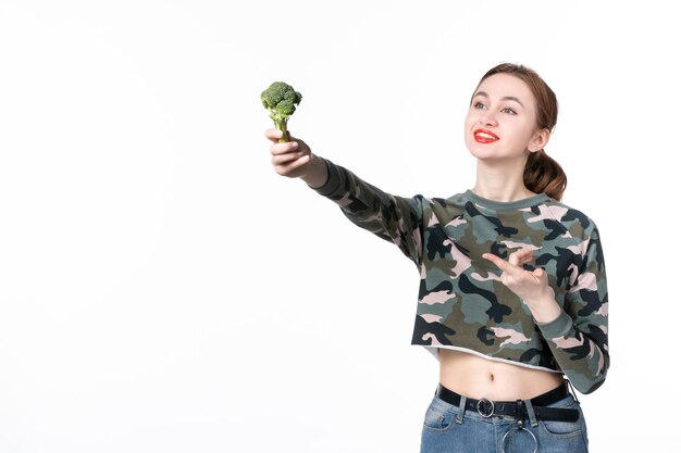 Vista frontale giovane femmina che tiene piccoli broccoli verdi su sfondo bianco pranzo pasto insalata cibo peso dieta umana assistenza sanitaria