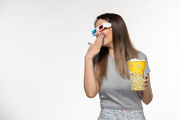 Vista frontale giovane femmina che tiene popcorn e guardare film in occhiali da sole d sulla superficie bianca chiara