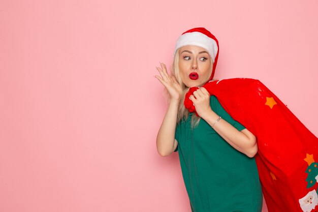 Vista frontale giovane femmina che trasporta borsa rossa con regali sulla parete rosa modello natale capodanno foto colore santa vacanze