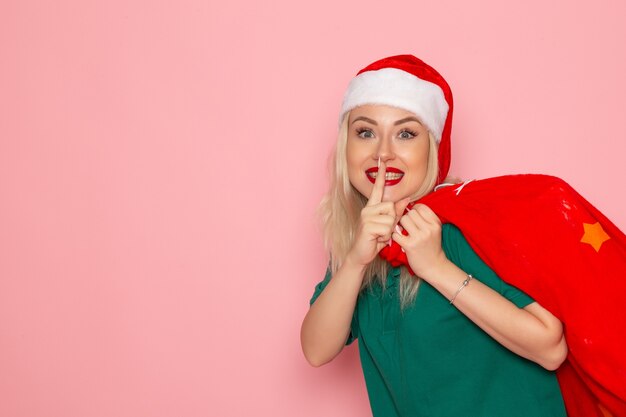 Vista frontale giovane femmina che trasportano borsa rossa con regali sulla parete rosa natale capodanno foto colore santa vacanza