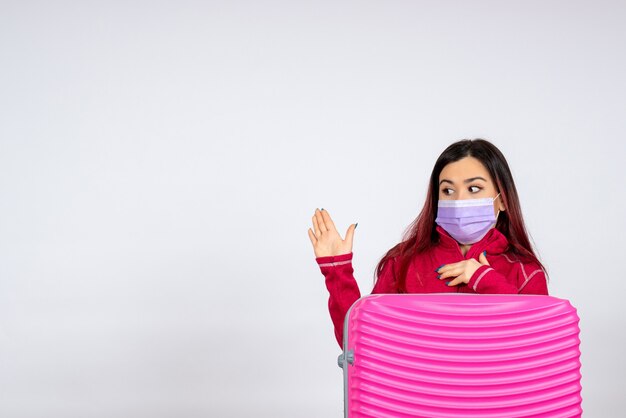 Vista frontale giovane femmina con borsa rosa in maschera sul muro bianco donna pandemia viaggio covid-virus colore