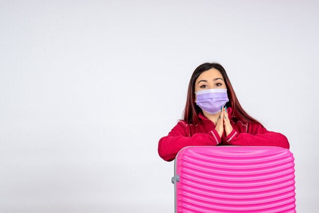 Vista frontale giovane femmina con borsa rosa in maschera sul muro bianco donna vacanza covid- viaggio pandemia virus colore