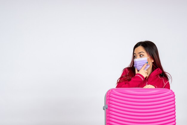 Vista frontale giovane femmina con borsa rosa in maschera sul muro bianco pandemia virus donna vacanza covid- viaggio di colore