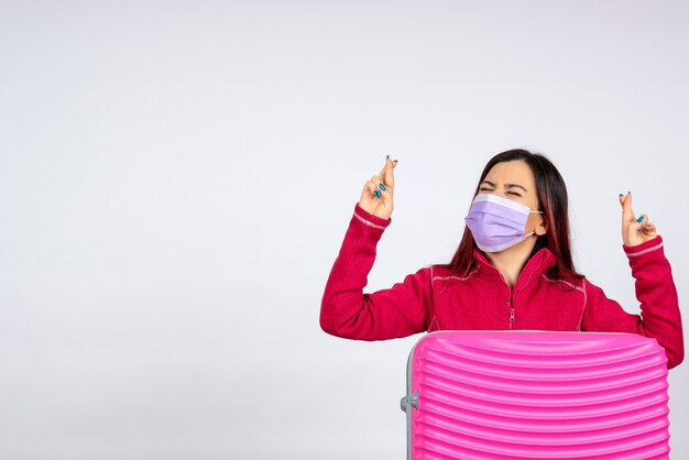 Vista frontale giovane femmina con borsa rosa in maschera sulla parete bianca vacanza pandemia virus covid- colori viaggio donna