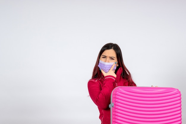 Vista frontale giovane femmina con borsa rosa in maschera sulla parete bianca vacanza virus covid colore viaggio pandemico donna