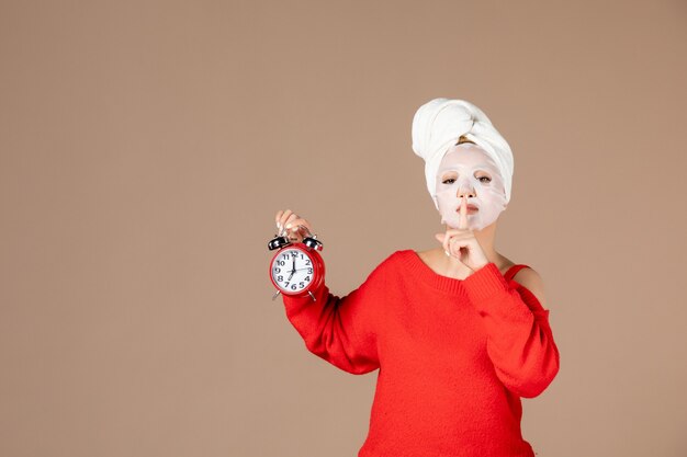 vista frontale giovane femmina con maschera facciale tenendo l'orologio su sfondo rosa