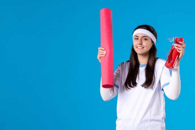 Vista frontale giovane femmina con materassino yoga sulla parete blu