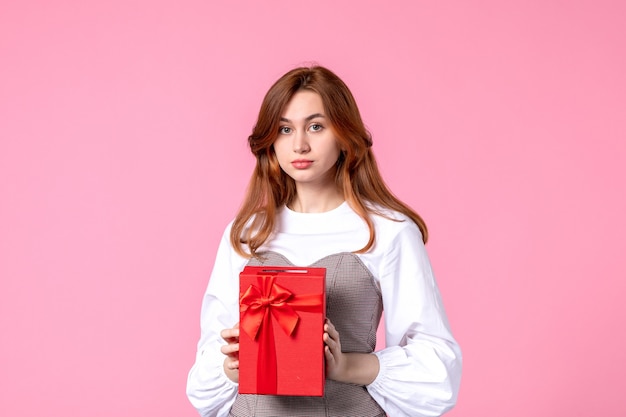 Vista frontale giovane femmina con presente nel pacchetto rosso su sfondo rosa marzo orizzontale sensuale regalo profumo foto donna parità di denaro