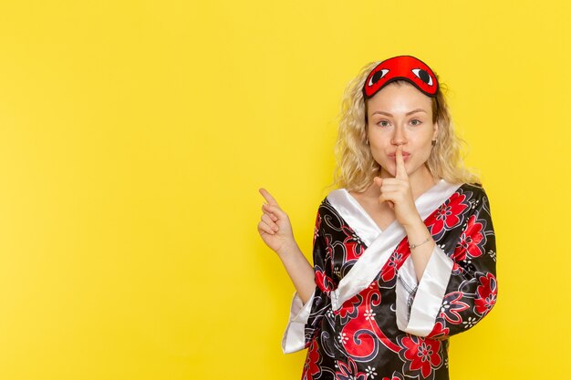 Vista frontale giovane femmina in abito da notte e indossa la maschera per gli occhi si prepara a dormire sul muro giallo notte sonno oscurità femminile colore