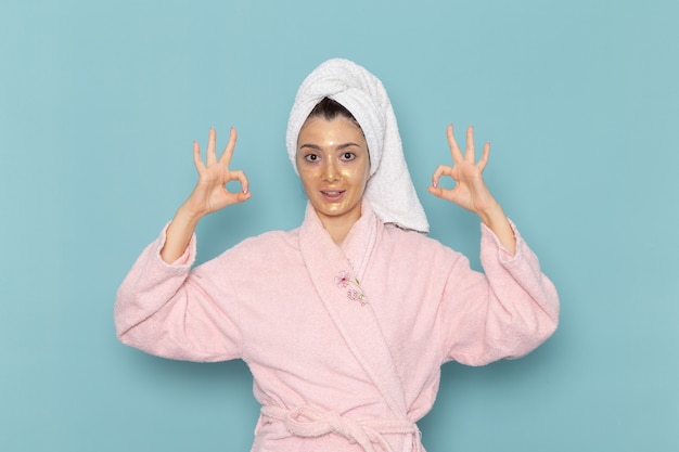Vista frontale giovane femmina in accappatoio rosa dopo la doccia sulla parete blu pulizia bellezza acqua pulita doccia crema selfcare
