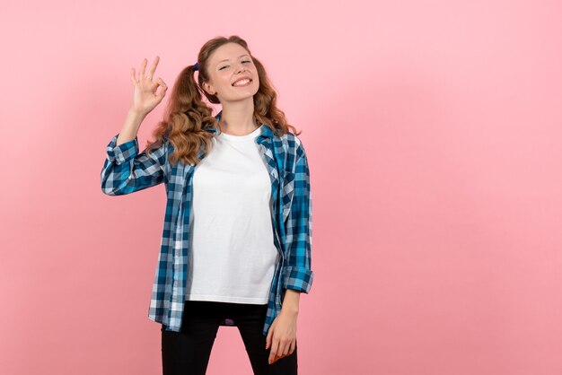 Vista frontale giovane femmina in camicia a scacchi in posa con un sorriso su sfondo rosa gioventù donna emozioni modello kid colore