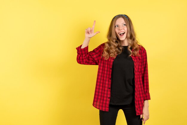 Vista frontale giovane femmina in camicia a scacchi rossa in posa con il sorriso su sfondo giallo emozione umana modello di colore donna