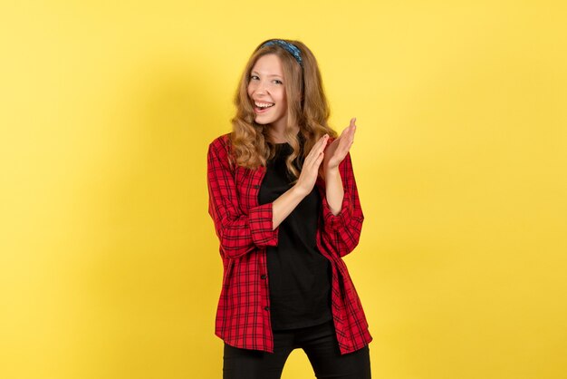 Vista frontale giovane femmina in camicia a scacchi rossa in posa con il sorriso su sfondo giallo emozione umana modello di colore donna