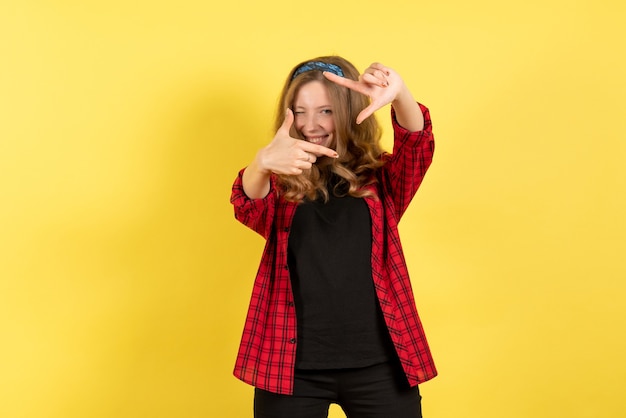 Vista frontale giovane femmina in camicia a scacchi rossa in posa con il sorriso su sfondo giallo ragazza umana emozione modello di colore donna