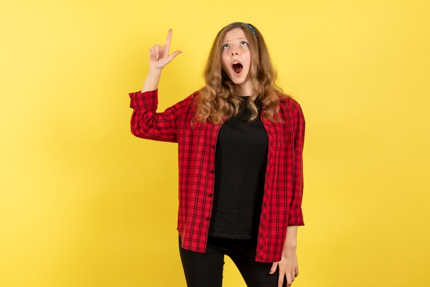 Vista frontale giovane femmina in camicia a scacchi rossa in posa e guardando il soffitto su sfondo giallo ragazze donna emozioni modello colore umano