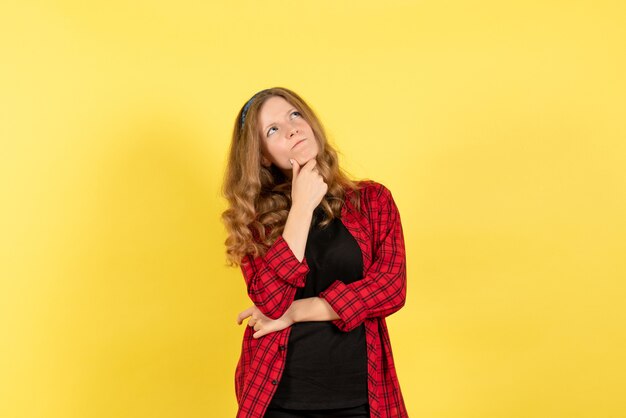 Vista frontale giovane femmina in camicia a scacchi rossa in posa e pensando su sfondo giallo donna emozione umana modello moda ragazza