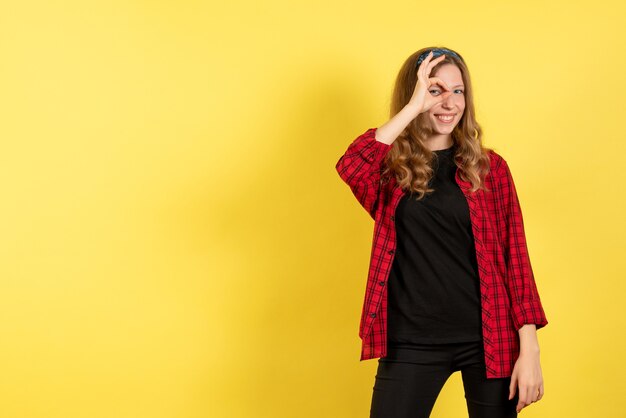 Vista frontale giovane femmina in camicia a scacchi rossa in posa e sorridente su sfondo giallo ragazza umana emozione modello di colore donna