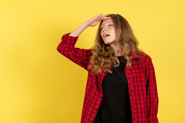 Vista frontale giovane femmina in camicia a scacchi rossa in posa guardando a distanza su sfondo giallo modello ragazze donna colore emozioni umane